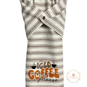 One stay put kitchen towel with brown stripes on an ivory background. The towel has the text 'Iced Coffee Please' printed on the front of the towel in orange and brown lettering with a black coffee cup on each side of the text. The towel has a snap closure so it can stay in place on an oven/stove/dishwasher handle. This listing is for one towel and includes free shipping.