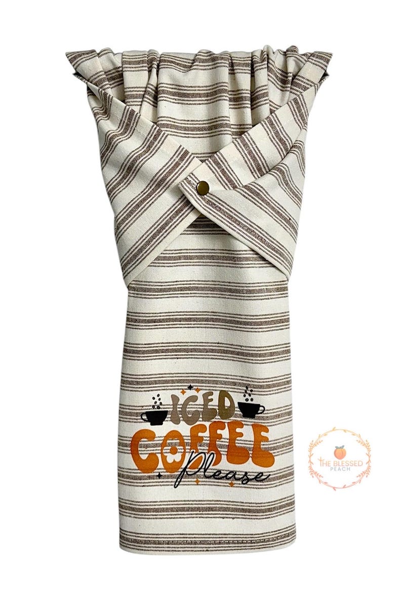 One stay put kitchen towel with brown stripes on an ivory background. The towel has the text 'Iced Coffee Please' printed on the front of the towel in orange and brown lettering with a black coffee cup on each side of the text. The towel has a snap closure so it can stay in place on an oven/stove/dishwasher handle. This listing is for one towel and includes free shipping.