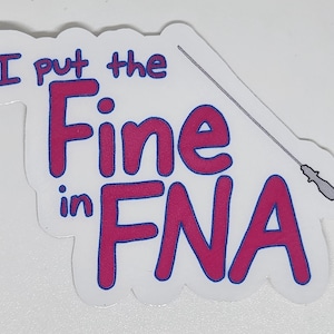May include: A white sticker with the text "I put the Fine in FNA" in pink letters with a blue outline. A medical needle is drawn above the text. The sticker is likely for medical professionals.