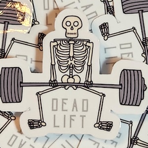 May include: A sticker featuring a cartoon skeleton lifting a barbell. The skeleton is white with black outlines, and the barbell has gray weights. The text "DEAD LIFT" is printed below the barbell in gray letters. The sticker is on a white background.