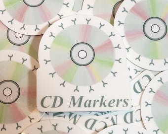 May include: CD markers with a colorful design. The markers have a white background with a circular design in the center, featuring a gradient of pink, green, and yellow. The text "CD Markers" is printed on the front.