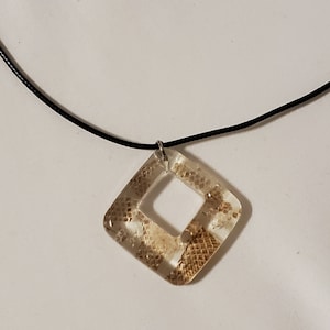 May include: A clear resin pendant necklace with a diamond shape. The pendant has a snakeskin pattern in shades of brown and tan. The necklace has a black cord.