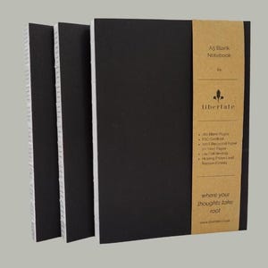May include: Three A5 blank notebooks with black covers and white-edged pages. The front notebook has a brown paper band with the text "A5 Blank Notebook" and "libertate". The band also lists features and the phrase "where your thoughts take root".