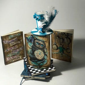 Könnte beinhalten: Ein Set aus vier kleinen, dekorativen Büchern mit einem skurrilen Alice-im-Wunderland-Thema. Die Bücher zeigen Illustrationen der Grinsekatze, des Weißen Kaninchens und einer Uhr. Die Bücher sind übereinander gestapelt, und ein Miniatur-Zylinderhut mit einer weißen Feder sitzt oben auf dem Stapel.