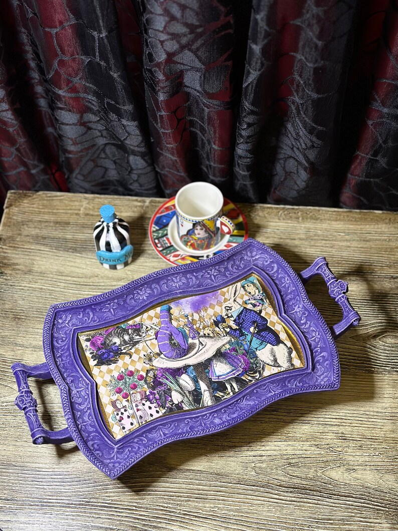 May include: Purple serving tray with ornate floral design and a whimsical Alice in Wonderland scene featuring the Mad Hatter, the White Rabbit, and Alice. The tray has two handles and is perfect for serving tea or snacks.