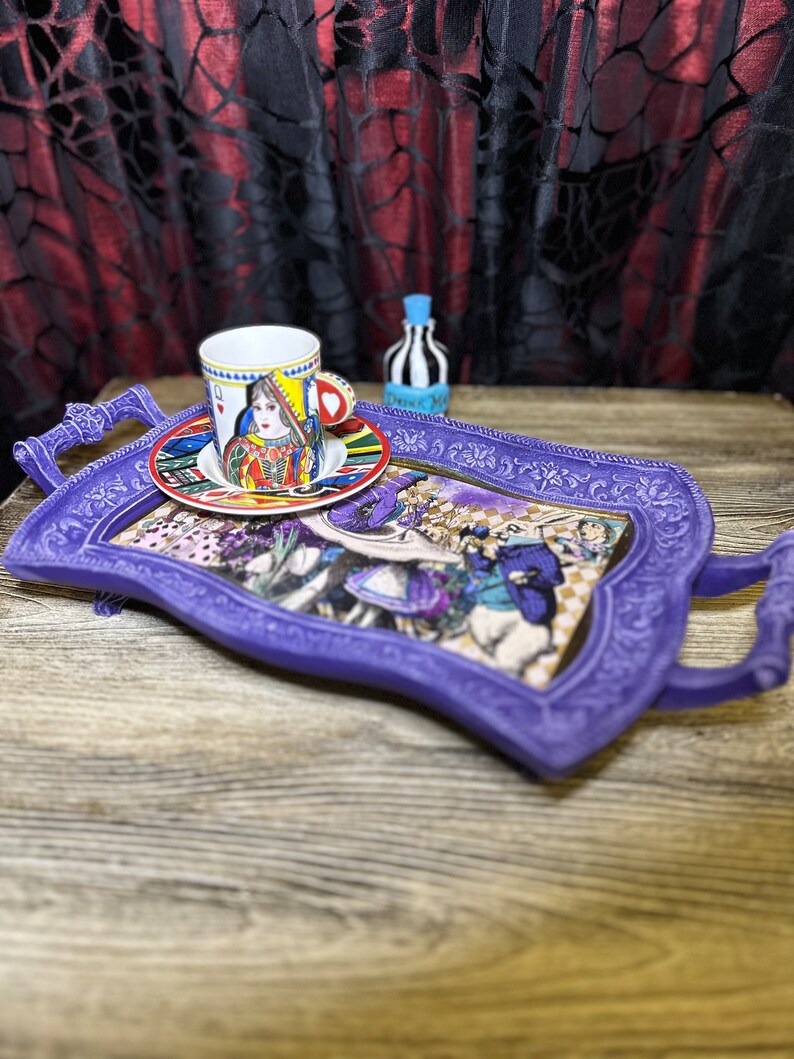 May include: A purple serving tray with a whimsical Alice in Wonderland design. The tray features a teacup with a Queen of Hearts design and a small bottle with a striped design.