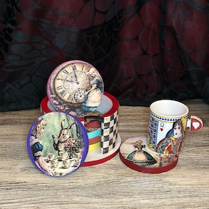 Può includere: Set di sei sottobicchieri colorati con illustrazioni a tema Alice nel Paese delle Meraviglie. I sottobicchieri sono rotondi e hanno un motivo a scacchi rosso, bianco e blu sul fondo. I sottobicchieri sono impilati uno sopra l'altro, con una tazza bianca con un design della Regina di Cuori sulla parte superiore. La tazza ha un manico a forma di cuore rosso.