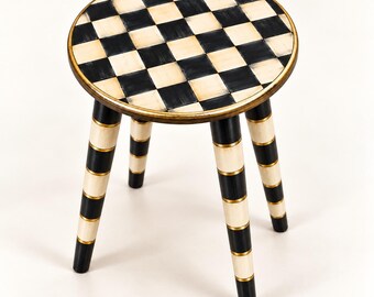 Taburete a cuadros negros y crema, asiento redondo con detalles en oro antiguo.