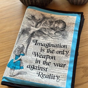 May include: A blue and black fabric journal cover with a quote from Alice in Wonderland: "Imagination is the only weapon in the war against Reality."