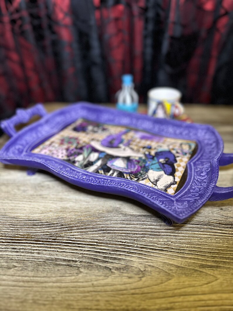 May include: A purple tray with an ornate design and a vintage illustration of a woman in a hat. The tray is on a wooden surface.