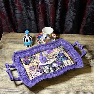 May include: Purple serving tray with a whimsical Alice in Wonderland design featuring the Mad Hatter, the White Rabbit, and Alice. The tray has two handles and a decorative border.