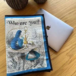 May include: A blue and black laptop sleeve with a vintage book page design featuring an illustration of Alice in Wonderland and the text "Who are you?"