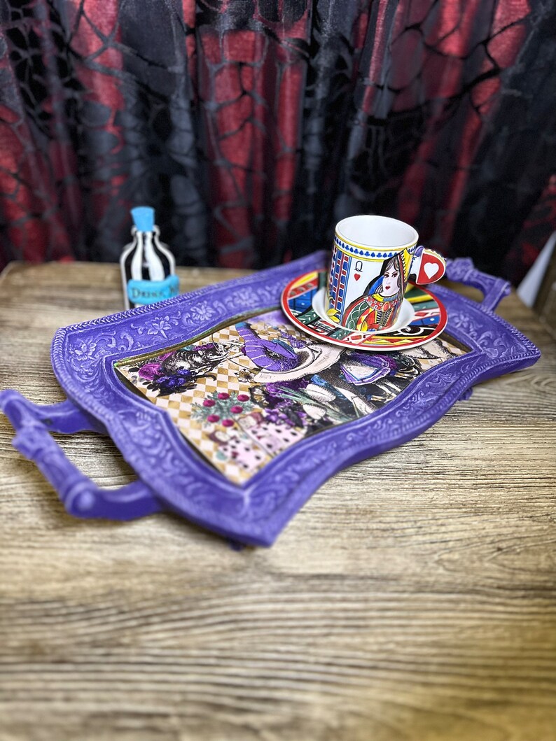 May include: Purple serving tray with ornate detailing and a whimsical Alice in Wonderland design. The tray features a teacup and saucer with a Queen of Hearts design.