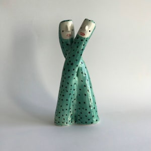 May include: Two ceramic figures, intertwined and facing each other, are green with black polka dots. The figures have white faces with painted features.