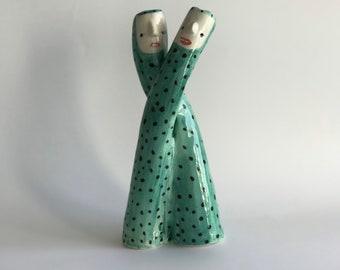 Puede incluir: Dos figuras de cerámica, entrelazadas y mirándose, son verdes con lunares negros. Las figuras tienen caras blancas con rasgos pintados.