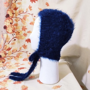 May include: A dark blue fuzzy knit hat with a long tie. The hat is on a white mannequin head.
