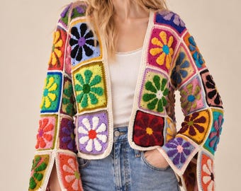Puede incluir: Un cárdigan de manga larga abierto por delante, confeccionado con cuadrados de ganchillo multicolores, cada uno con un motivo floral en relieve en tonos amarillo, rosa, azul, verde, morado y rojo, con ribete blanco y puños acampanados.