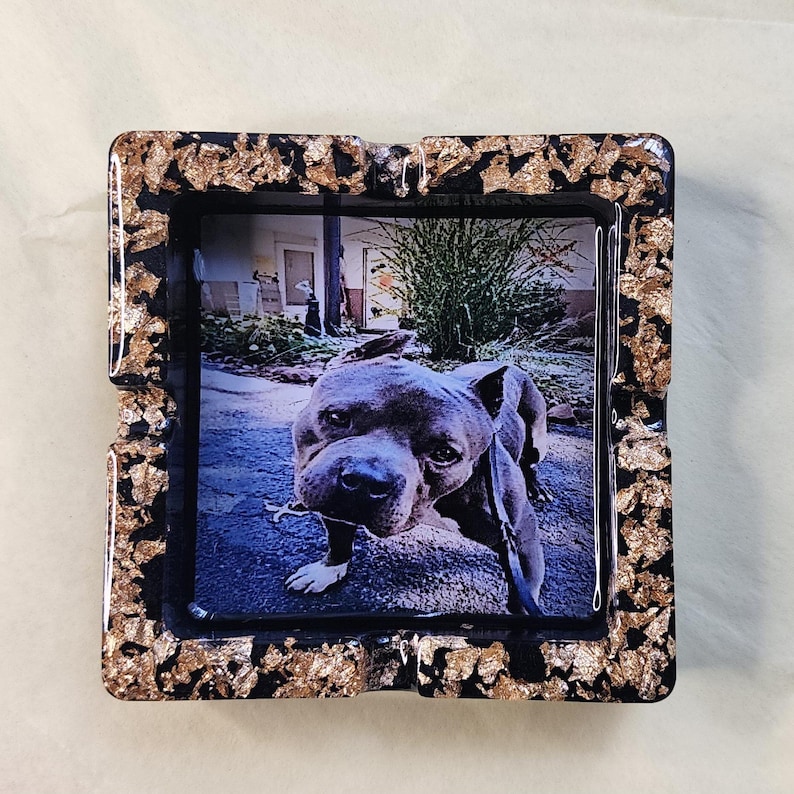 Op de afbeelding: Zwarte vierkante asbak met een bladgoud ontwerp. De asbak heeft een afbeelding van een grijze pitbull-hond erin.