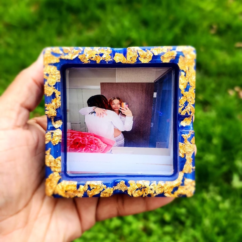 Op de afbeelding: Een blauwe en gouden harsbak met een foto van een stel erin. De foto toont twee mensen die elkaar omhelzen en lachen. De bak heeft een gouden bladontwerp rond de randen.