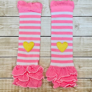 May include: A pair of pink and white striped leg warmers with a yellow heart on each. The leg warmers have a ruffled edge.