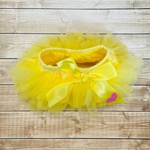 May include: A yellow tulle tutu with a yellow satin bow and a pink glitter heart.