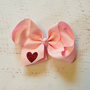May include: A pink hair bow with a red glitter heart in the center.