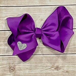 May include: A large purple hair bow with a sparkly silver heart in the center.