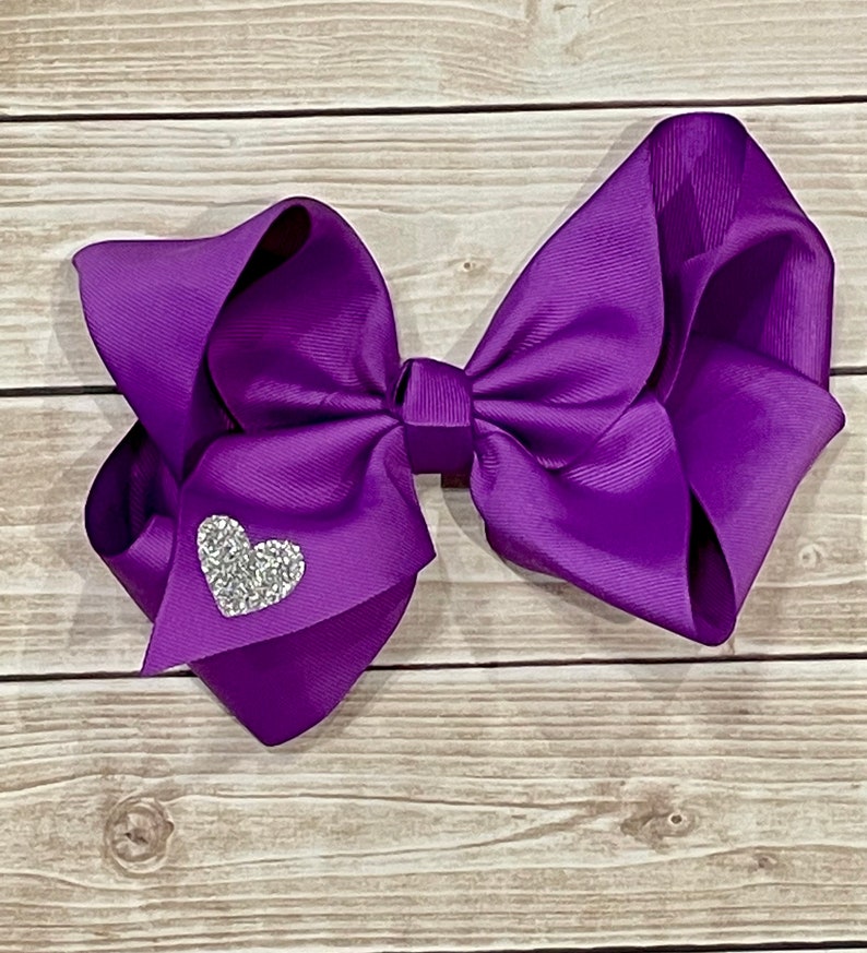 May include: A large purple hair bow with a sparkly silver heart in the center.