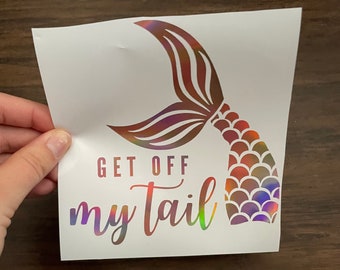 May include: A white sticker with a holographic mermaid tail and the text "Get off my tail".