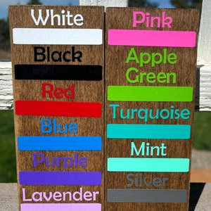 May include: Two wooden signs with color swatches and names. The left sign has the colors white, black, red, blue, purple, and lavender. The right sign has the colors pink, apple green, turquoise, mint, and silver.