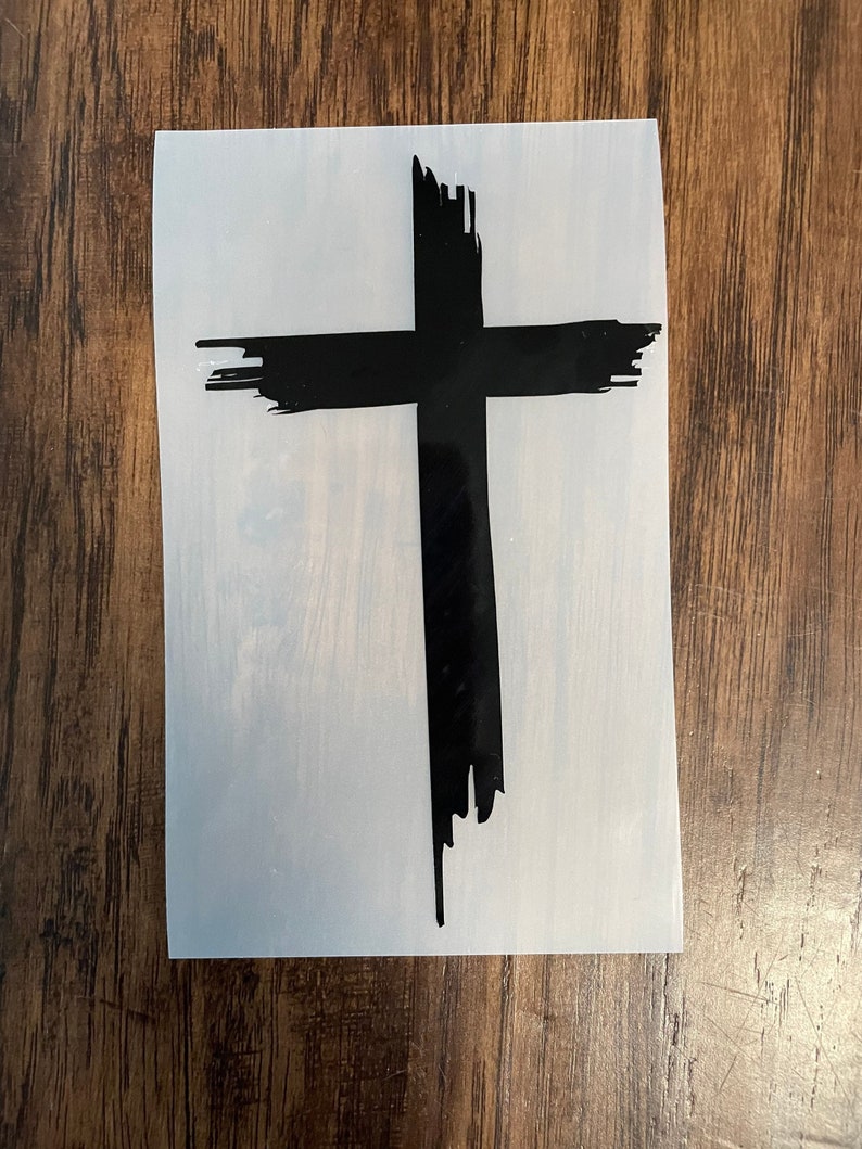 May include: A black cross with a distressed, brushstroke design. The cross is on a white background.