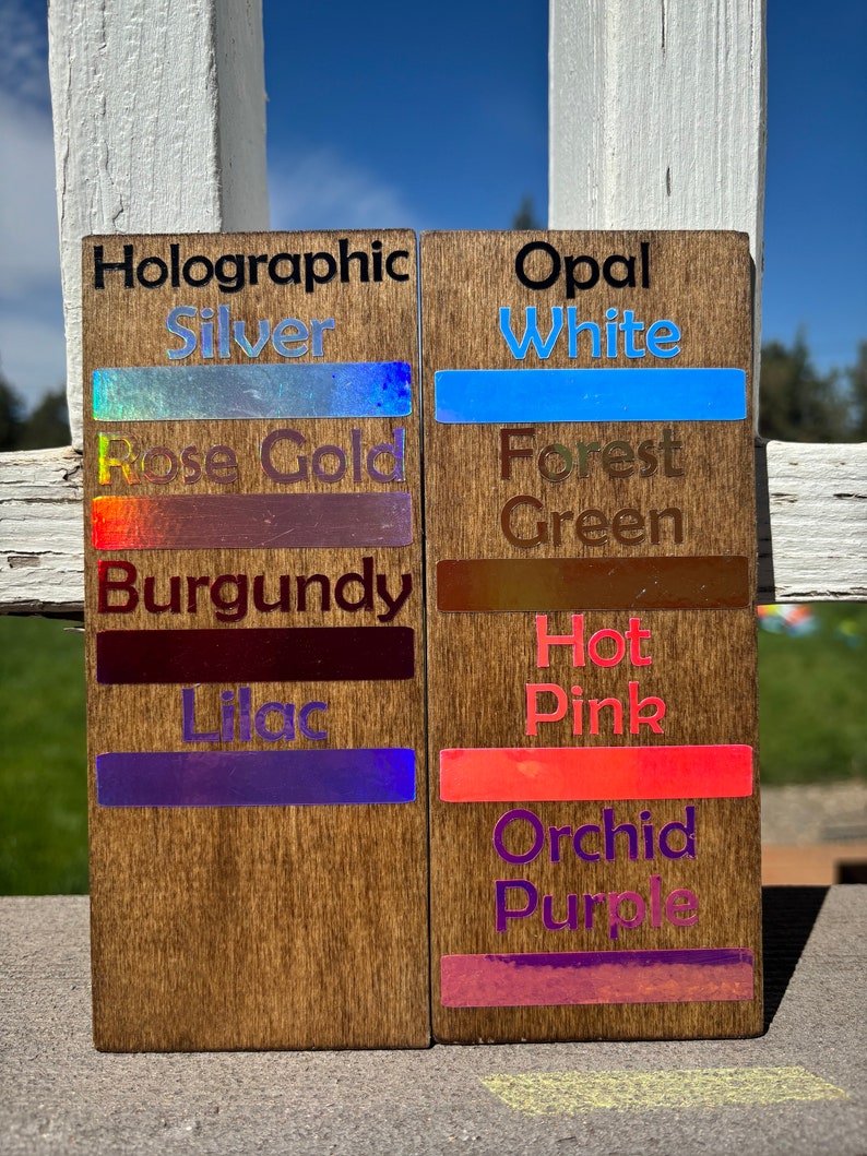 May include: Two wooden signs with different holographic and opal finishes. The left sign has the text "Holographic" and lists the colors "Silver", "Rose Gold", "Burgundy", and "Lilac". The right sign has the text "Opal" and lists the colors "White", "Forest Green", "Hot Pink", and "Orchid Purple".