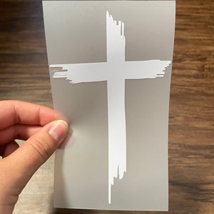May include: White vinyl decal of a cross with a distressed paint effect.