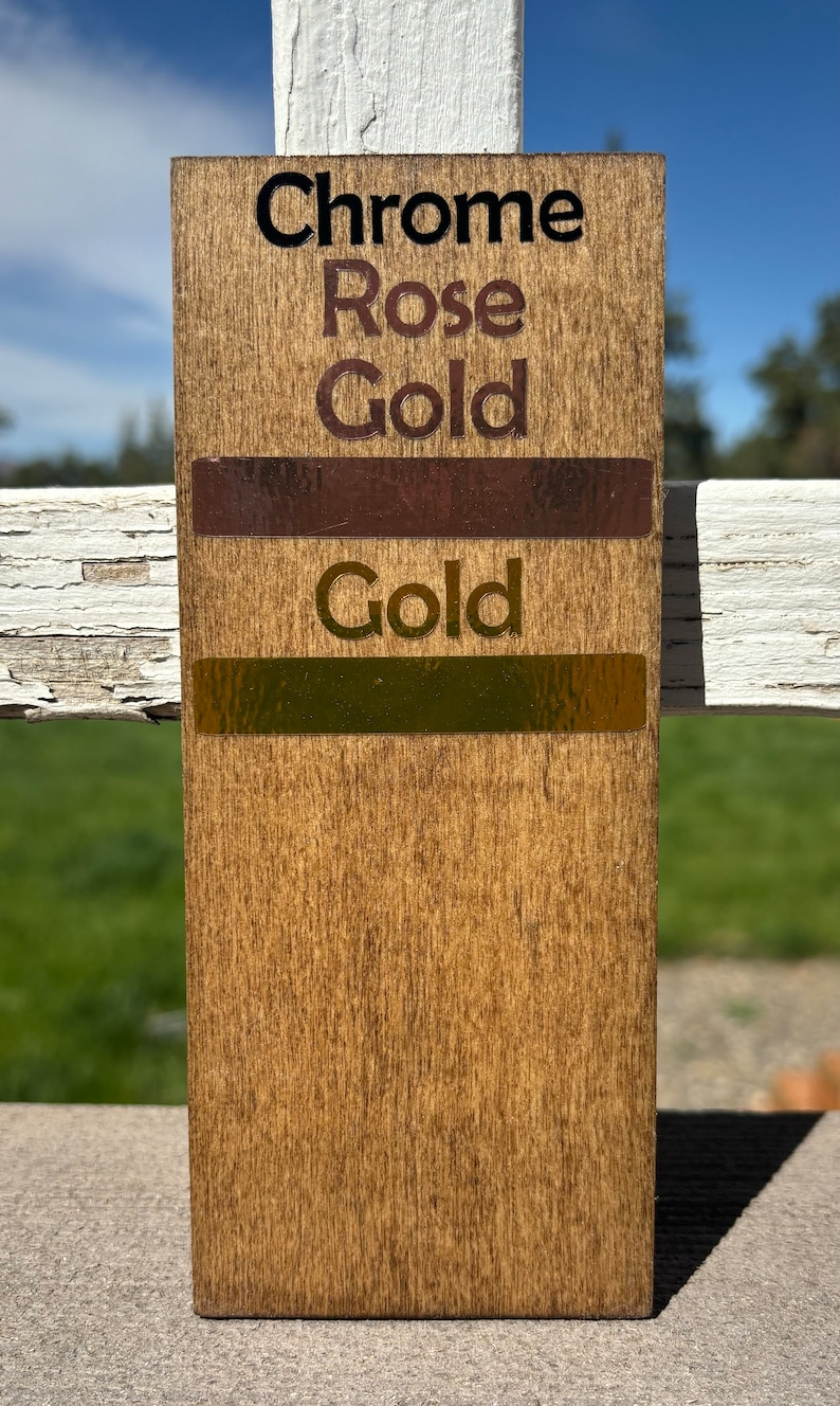 May include: A wooden sample board with three swatches of metallic paint. The top swatch is labeled "Chrome Rose Gold", the middle swatch is labeled "Gold", and the bottom swatch is labeled "Gold".