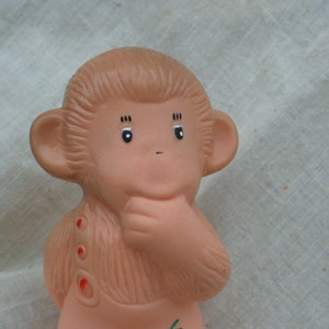 Puede incluir: Figura de mono vintage, marrón claro, con expresión pensativa. El mono tiene ojos negros, orejas pequeñas y se toca la boca con la mano. Acentos rojos en el pecho del mono. La figura probablemente sea de goma o plástico.
