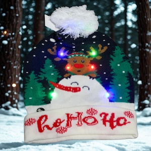 May include: A festive Christmas hat with a snowman and reindeer design, featuring LED lights. The hat has a white pom-pom and the words "Ho Ho Ho" in red. The background shows a snowy forest.