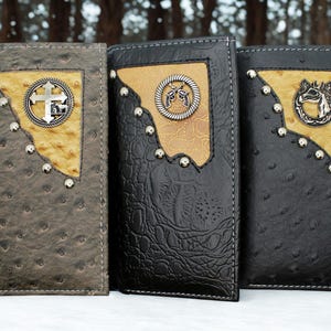 May include: Three leather wallets in shades of gray and black, each featuring a decorative emblem and silver studs. The wallets have a textured finish and a contrasting tan-colored patch.