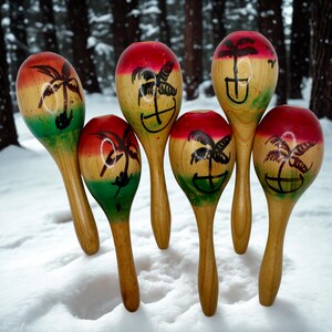 May include: A set of five wooden maracas featuring a natural wood handle and a rounded top painted with horizontal bands of red, yellow, and green. Each maraca is decorated with a black hand-painted palm tree silhouette on the upper portion.