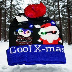 May include: Black knit winter hat with a blue brim and a red pom-pom. The hat features light-up designs of an owl and Santa Claus, with the text "Cool X-mas" in white letters on the brim. The background is a snowy forest.