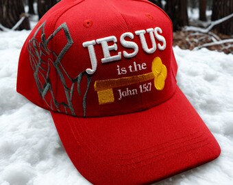 May include: A red baseball cap with the words "JESUS is the John 15:7" embroidered in white and gold. The cap has a curved brim and a gray design on the side.