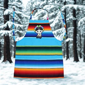 May include: A vibrant apron in a traditional Mexican serape style. The apron has a light blue base with horizontal stripes in shades of red, orange, green, and blue. A small embroidered doll is featured in the center of the apron.