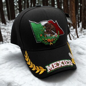 May include: Black baseball cap featuring the Mexican flag embroidered on the front. The flag design includes green, white, and red colors, with an eagle emblem. The word "MEXICO" is embroidered in white with a green border on the brim, along with a gold laurel wreath.