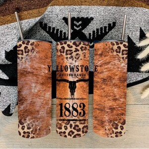 May include: Three stainless steel tumblers with a brown and tan cowhide pattern and leopard print accents. The middle tumbler has the text "Yellowstone Dutton Ranch 1883" printed on it.