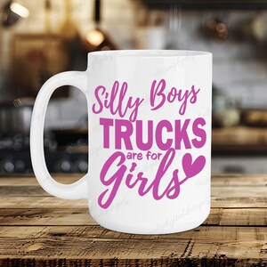 Op de afbeelding: Witte keramische mok met een roze ontwerp met de tekst "Silly Boys Trucks are for Girls" met een roze hart.