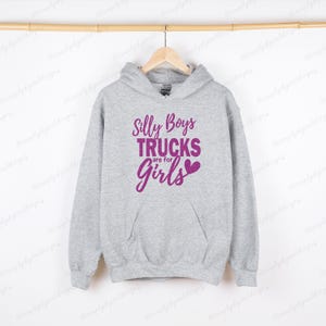 Op de afbeelding: Een grijs hoodie met een roze afbeelding met de tekst "Silly Boys Trucks are for Girls" met een roze hart.