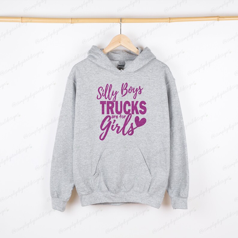 Op de afbeelding: Een grijs hoodie met een roze afbeelding met de tekst "Silly Boys Trucks are for Girls" met een roze hart.