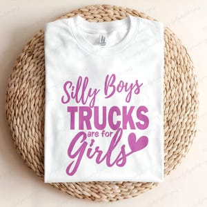 Op de afbeelding: Wit T-shirt met roze tekst die "Silly Boys Trucks are for Girls" met een roze hartje zegt.