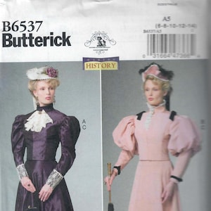 May include: A vintage sewing pattern for a long, full-skirted dress with a high neck and puffed sleeves. The pattern is from Butterick and is for sizes 6-8-10-12-14. The pattern is called "Making History" and is for a dress with a lace trim.