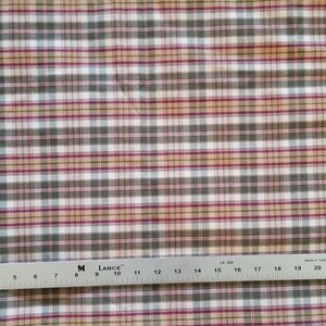 May include: A close-up of a white fabric with a plaid pattern in shades of red, green, and beige. The fabric is measured with a ruler, showing a length of 61 cm.
