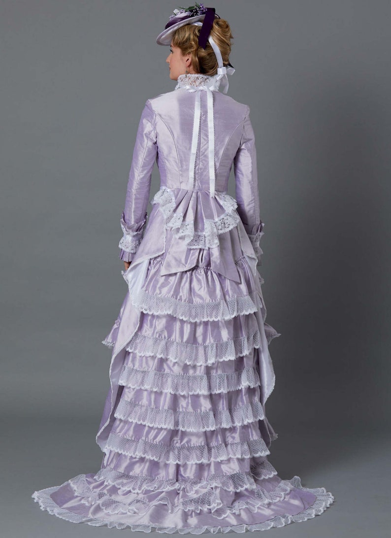 May include: A lavender gown with a white lace trim and a ruffled skirt. The gown has a fitted bodice with a high neckline and long sleeves. The gown is worn by a woman with a hat and gloves.